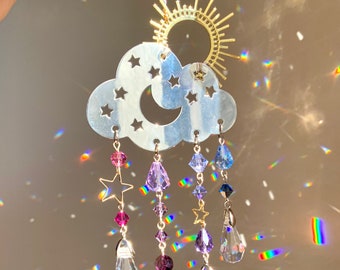 Puede incluir: Un atrapasol de nube plateado con una luna creciente y estrellas recortadas. Tiene cinco hilos de cristales colgando de él, cada uno con un amuleto de estrella y un cristal en forma de lágrima.