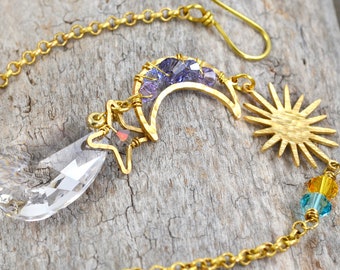 May include: A gold chain with a crystal prism, a sun, a crescent moon with purple crystals, and a star charm.