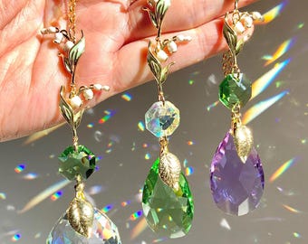 Puede incluir: Tres pendientes de cadena dorada con abalorios de lirio de los valles y gotas de cristal. Los cristales son transparentes, verdes y morados.