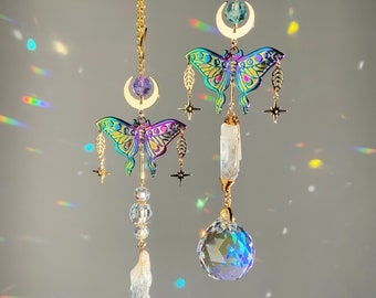 Puede incluir: Dos encantos de mariposa iridiscentes colgando de cadenas doradas con acentos de cristal. Cada encanto presenta una luna creciente y una punta de cristal. Un encanto tiene una bola de cristal transparente colgando de él.