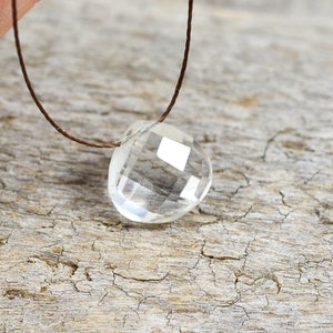 Puede incluir: Un colgante de cristal de cuarzo transparente en un collar de cordón marrón.