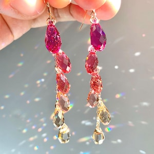 May include: A pair of dangle earrings with a gradient of pink, red, and gold teardrop-shaped crystals.