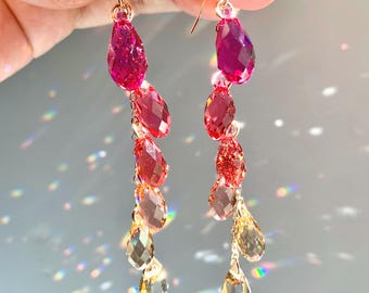 Könnte beinhalten: Ein Paar Ohrringe mit einem Farbverlauf aus rosa, roten und goldenen tropfenförmigen Kristallen.