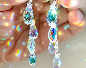 May include: A pair of dangling earrings featuring multiple faceted, clear crystal teardrop beads that reflect vibrant rainbow light. The crystals are arranged in a vertical chain pattern and are attached to silver-toned metal earring hooks.