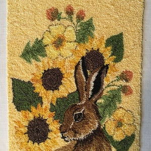 May include: A textured wall hanging depicting a brown hare with sunflowers and foliage. The artwork uses shades of yellow, green, brown, and orange. The design is rustic and nature-inspired, perfect for adding a touch of the countryside to any room.
