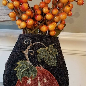May include: A black and orange needlepoint pumpkin with a smiling face, in a black fabric bag, with a bunch of orange berries on top.