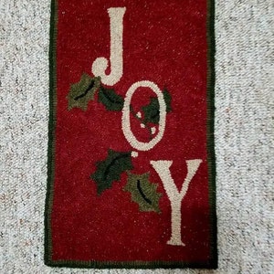 May include: A red and green rug with the word "JOY" in white lettering. The letters are surrounded by green holly leaves.