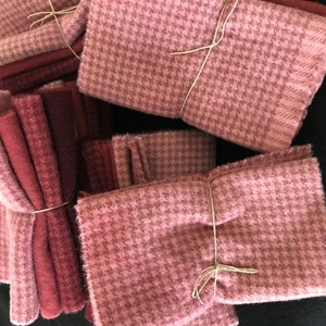 May include: A stack of pink and red wool fabric squares, tied together with twine. The fabric has a houndstooth pattern.