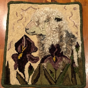 May include: A hand-stitched rug depicting a white fluffy lamb with a purple and yellow iris flower in the foreground. The rug has a green border.
