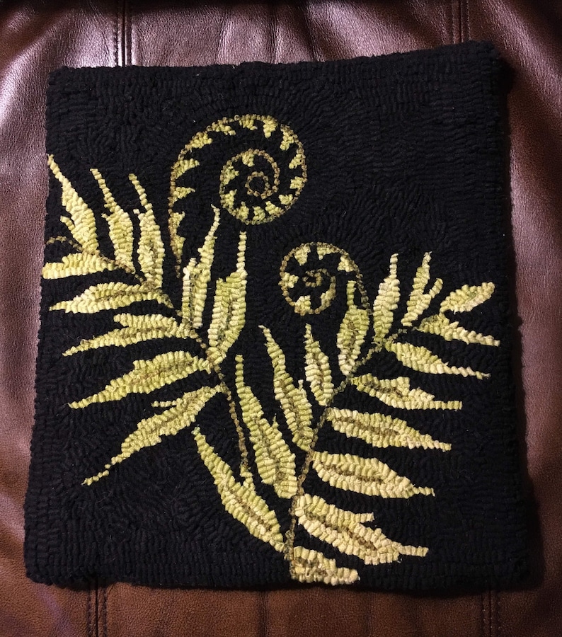 May include: A black and gold rug with a fern design. The fern is made up of small, individual loops of yarn.