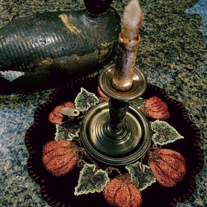 May include: A dark brown, wooden, duck decoy sits on a black and red, hand-stitched, pumpkin-themed, needlepoint rug with a brass candle holder and a white candle.