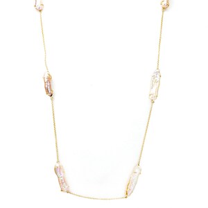 May include: A long gold chain necklace with five irregular shaped pearls. The pearls are a mix of white and pink.