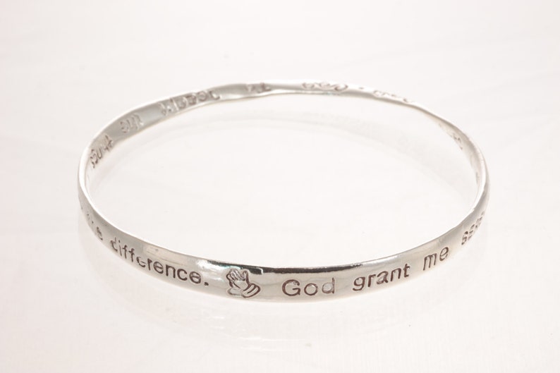 May include: Silver bangle bracelet with the inscription "God grant me the serenity to accept the things I cannot change, courage to change the things I can, and wisdom to know the difference."