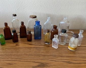 May include: A collection of vintage glass bottles in various colors and sizes. The bottles are clear, amber, blue, and green. Some of the bottles have cork stoppers, while others have metal lids. The bottles are arranged on a wooden surface.