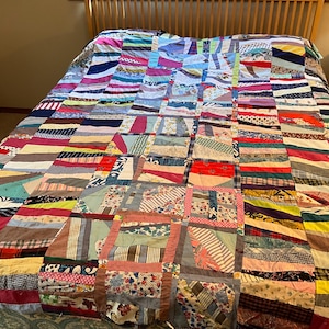 May include: A patchwork quilt featuring a chaotic arrangement of rectangular fabric scraps in various colors, patterns, and textures, including stripes, florals, polka dots, and solid hues, stitched together in a multi-directional block design.