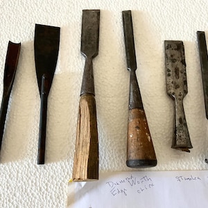 May include: A collection of six vintage wood chisels with metal blades and wooden handles. The chisels vary in size and shape, with some having straight edges and others curved. The tools are arranged on a white surface.