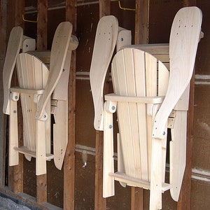 Puede incluir: Dos sillas plegables de madera sin terminar est&aacute;n colgadas en una pared. Las sillas son de madera natural y tienen un dise&ntilde;o sencillo.