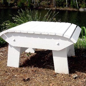 May include: White wooden outdoor bench with a curved top and four legs. The bench is sitting on a bed of brown pine needles.