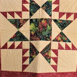 May include: A handmade quilt with a starburst design. The quilt features a central square with a floral pattern, surrounded by cream-colored triangles and burgundy accents. The border is burgundy with a small star pattern.