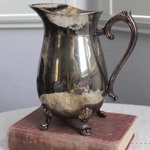 May include: A white ceramic mug with a black handle and the text "But First, Coffee" in a handwritten style. The mug is on a white surface. The mug is 4 inches tall.