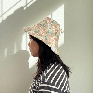 May include: A floral print sun hat with a cream-colored base, adorned with red and blue flower patterns. The hat has a wide brim and is worn by a person wearing a black and white striped shirt.