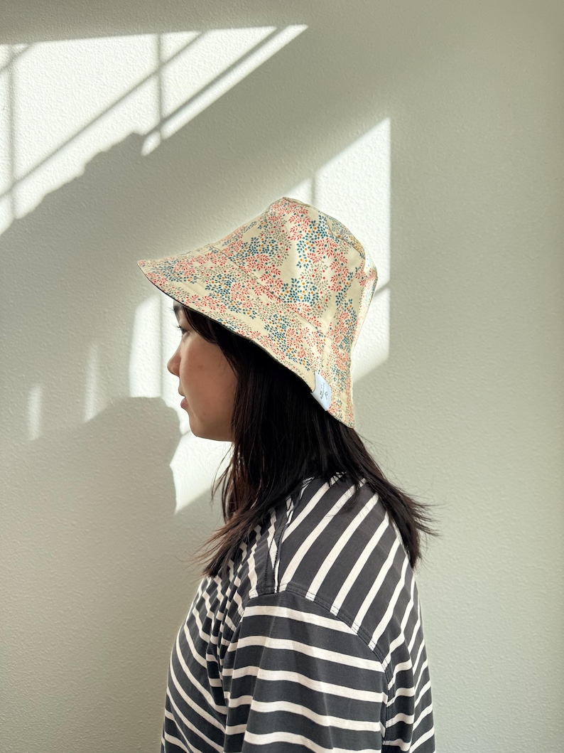 May include: A floral print sun hat with a cream-colored base, adorned with red and blue flower patterns. The hat has a wide brim and is worn by a person wearing a black and white striped shirt.