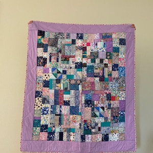 May include: A patchwork quilt with a purple border and a variety of floral and geometric patterns in shades of blue, pink, and white.