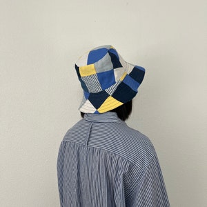 May include: A blue and yellow patchwork bucket hat with a wide brim. The hat is made of different fabrics and has a geometric pattern.
