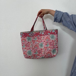 K&ouml;nnte beinhalten: Eine rote und wei&szlig;e Tragetasche mit Blumenmuster. Die Tasche hat zwei Henkel und ist aus Stoff.