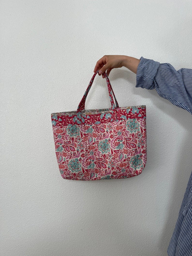 K&ouml;nnte beinhalten: Eine rote und wei&szlig;e Tragetasche mit Blumenmuster. Die Tasche hat zwei Henkel und ist aus Stoff.