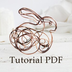 May include: A copper wire sculpture of a rabbit with white beads. The sculpture is on a white wooden surface. The text "Tutorial PDF" is below the sculpture.