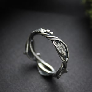 May include: A silver ring with a twisted vine design and a leaf detail. The ring is made of sterling silver and is a unique and delicate piece of jewelry.