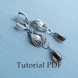 May include: A pair of silver earrings with a teardrop-shaped brown gemstone and a pearl hanging from each earring. The earrings are made with wire wrapped around the stones and pearls. The earrings are on a blue background. Tutorial PDF.
