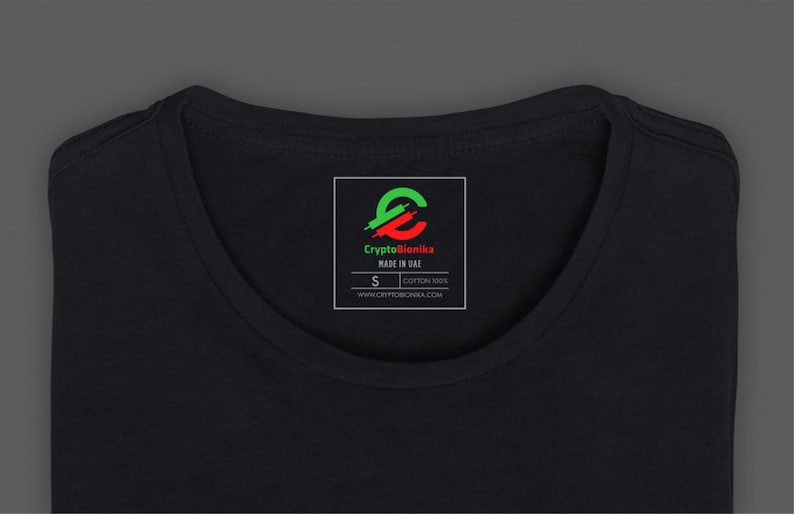 May include: Black t-shirt with a white tag that says "CryptoBionika" in red and green letters. The tag also includes a logo of a stylized letter "E" with a green and red design. The tag also says "Made in Italy" and "Cotton 100%". The tag also includes the size "S" and the website "www.cryptobionika.com".