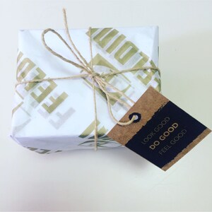 May include: A wrapped gift with white paper featuring a gold-colored repeating pattern. The package is tied with twine and has a brown tag with the words "LOOK GOOD DO GOOD FEEL GOOD" in gold lettering.