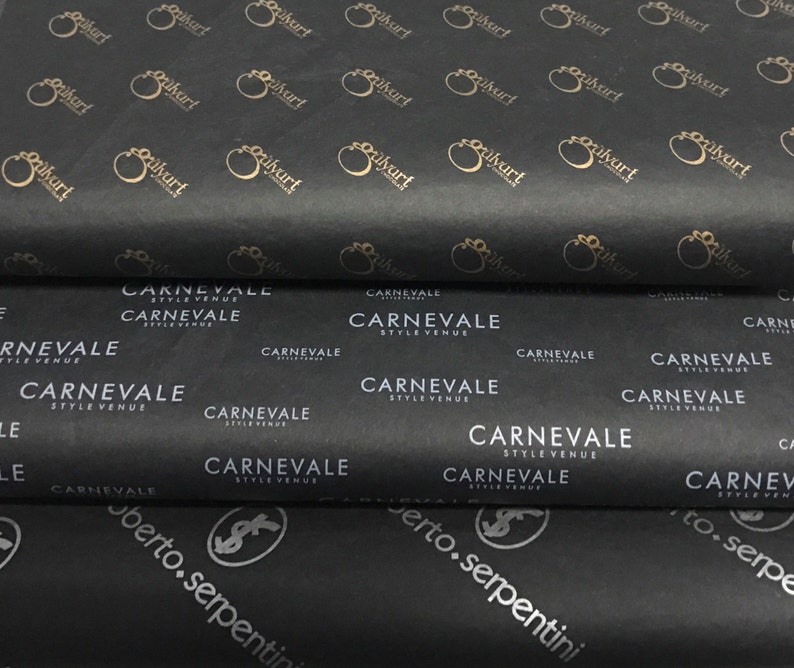 Puede incluir: Papel de seda negro con patrones de logotipos dorados repetidos y texto. El texto incluye "silvart", "CARNEVALE STYLE VENUE" y "roberto.serpentini". El papel est&aacute; doblado y apilado.