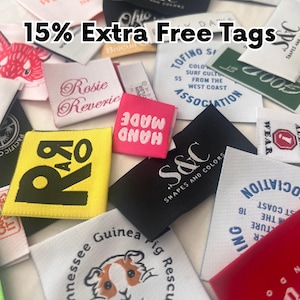 May include: A collection of assorted fabric clothing labels in various colours, shapes, and sizes. The tags feature diverse printed and embroidered logos, brand names, and graphic illustrations, including a guinea pig and text like 15% Extra Free Tags.