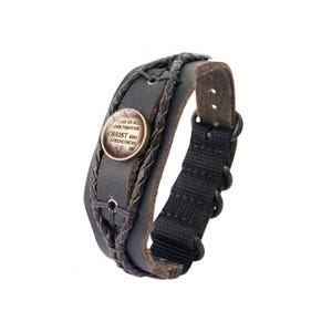 May include: A black leather bracelet with a braided design and a black fabric strap. The bracelet features a circular metal charm with the text "I CAN DO ALL THINGS THROUGH CHRIST WHO STRENGTHENS ME."