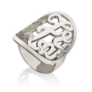 Op de afbeelding: Een zilverkleurige ring met een sierlijk, opengewerkt ontwerp. De ring heeft een grote, gebogen bovenkant met een wervelend patroon en een dikke band. De ring wordt getoond op een witte achtergrond, met een lichte reflectie.