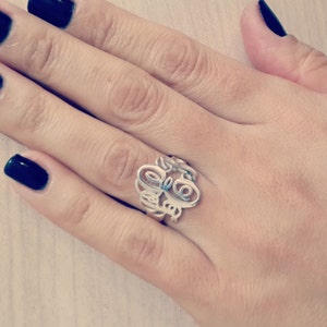 Peut inclure: Une bague en argent avec un motif de monogramme. La bague est sur le doigt d'une personne.