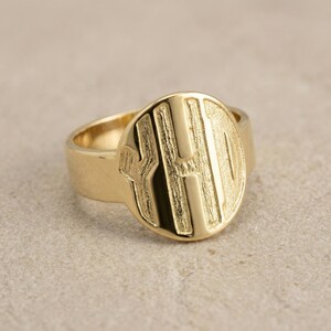 Op de afbeelding: Een goudkleurige zegelring met een grote, ronde voorkant. De voorkant heeft de letters "H O" in reli&euml;f in een vet, schreefloos lettertype. De ring heeft een dikke band en een gepolijste afwerking.
