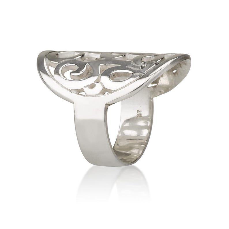 Op de afbeelding: Een zilveren ring met een open ontwerp. De ring heeft een brede, halvemaanvormige bovenkant met een wervelend filigraanpatroon. De band is effen en glad, tegen een witte achtergrond.