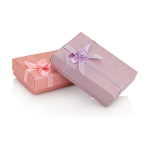 K&ouml;nnte beinhalten: Zwei kleine Geschenkboxen mit dekorativem Band und einem Blumenakzent. Die obere Box ist lavendelfarben mit einem lavendelfarbenen Band und die untere Box ist rosa mit einem rosafarbenen Band.