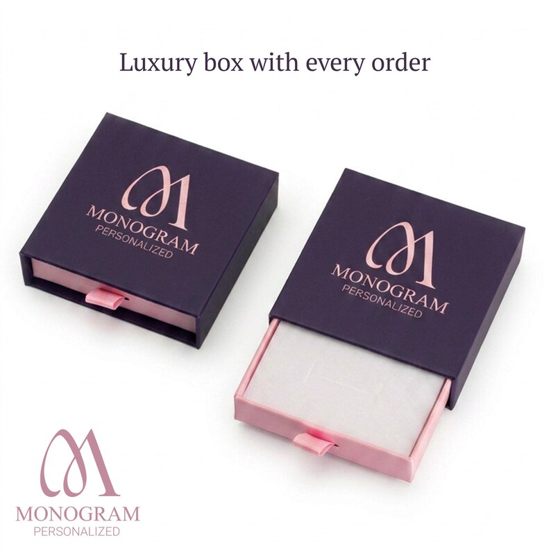 Op de afbeelding: Twee donkerpaarse geschenkdozen met roze interieurs en treklipjes. Elke doos heeft een ros&eacute;gouden monogramlogo en de woorden "MONOGRAM PERSONALIZED" op het deksel. De tekst "Luxury box with every order" staat erboven.