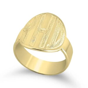 Op de afbeelding: Een goudkleurige zegelring met een gepolijste band en een ovale voorkant. De voorkant heeft de gegraveerde initialen "YHD" in een vetgedrukte, schreefloze letter. De ring is gemaakt van glanzend, reflecterend metaal.