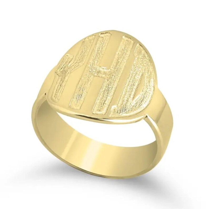 Op de afbeelding: Een goudkleurige zegelring met een gepolijste band en een ovale voorkant. De voorkant heeft de gegraveerde initialen "YHD" in een vetgedrukte, schreefloze letter. De ring is gemaakt van glanzend, reflecterend metaal.