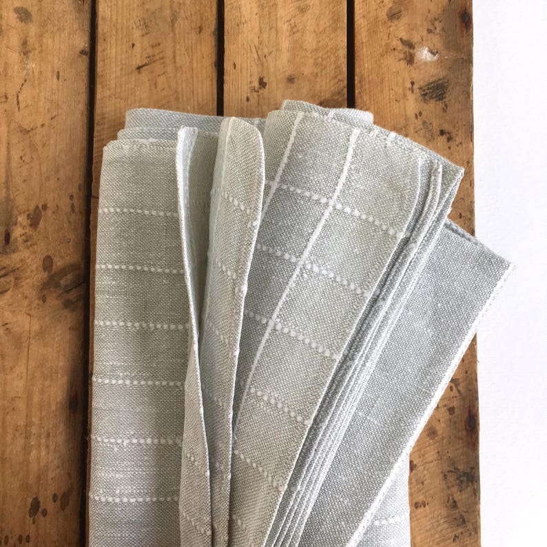 May include: A stack of gray linen napkins with a white dotted pattern. The napkins are folded and arranged on a wooden surface.