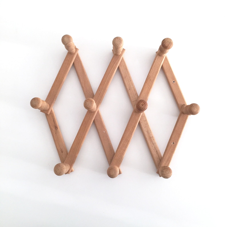 May include: A wooden coat rack with eight hooks, folded in a zig-zag pattern. The rack is made of light brown wood and has a natural finish.
