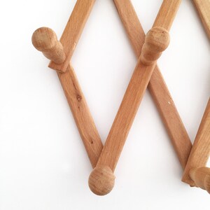May include: A wooden wall-mounted coat rack with a diamond pattern and rounded hooks. The rack is made of light brown wood and has a rustic look.