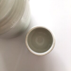 May include: White ceramic lid for a jar or container. The lid is round and has a smooth, slightly textured surface.